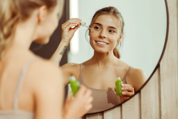 Woman applying skincare with a dropper, promoting fragrance-free products for sensitive skin in a mirror reflection.